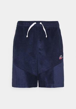 Marineblauwe corduroy korte broek met elastische tailleband, witte trekkoorden en klein rood Nike-logo op het linkerbeen.