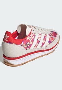 Röd och vit sportskor med blommönster, ovandel i mocka och syntetmaterial, gummisula och tre vita ränder på sidan.