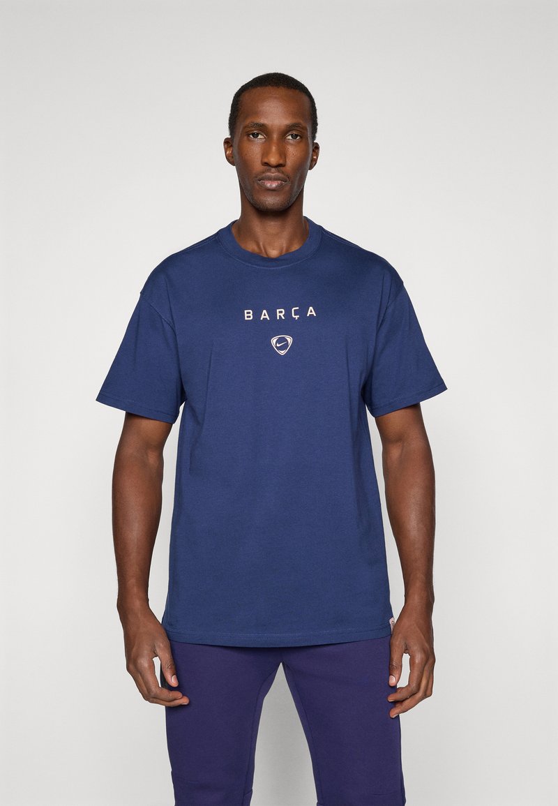 Marinblå bomulds t-shirt med korte ærmer, der pryder "BARÇA" og et Nike-logo i hvidt på brystet, rund halsudskæring.