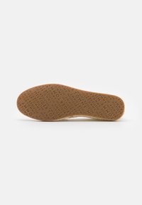 Semelle de chaussure en caoutchouc brun texturé avec motif de marque "Tommy Hilfiger" répété sur fond blanc.