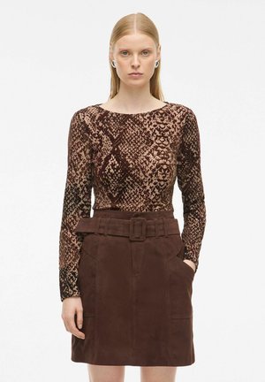 Langarmtop in bruin en beige slangenprint stof, gecombineerd met een hoge taille, bruine leren rok met riem en zijzakken.
