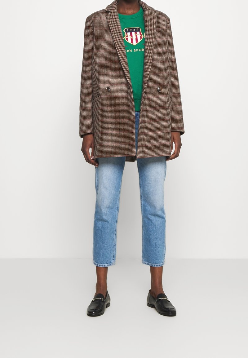 Bruine geruit oversized blazer met geknipte revers, dubbelzijdige knopen, gedragen over een groene graphic sweatshirt en lichtblauwe cropped jeans.