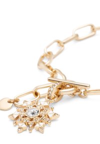 Gouden armband met een geometrische stervormige bedel met witte emaille en een centraal heldere edelsteen, bevestigd met een toggle-sluiting.