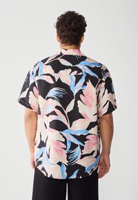 Short-sleeve shirt in lightweight fabric featuring a bold floral pattern in pink, blue, and cream on a black background. Flat collar and curved hem.