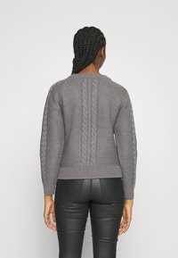 Pull en maille gris avec détails torsadés dans le dos et sur les manches, doté d'un col rond et d'un ourlet côtelé. Matière texturée et chaude.