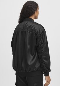 Jachetă bomber din satin negru, cu mâneci și tiv strâns, având o textură netedă și o croială lejeră. Design minimalist fără decorații.