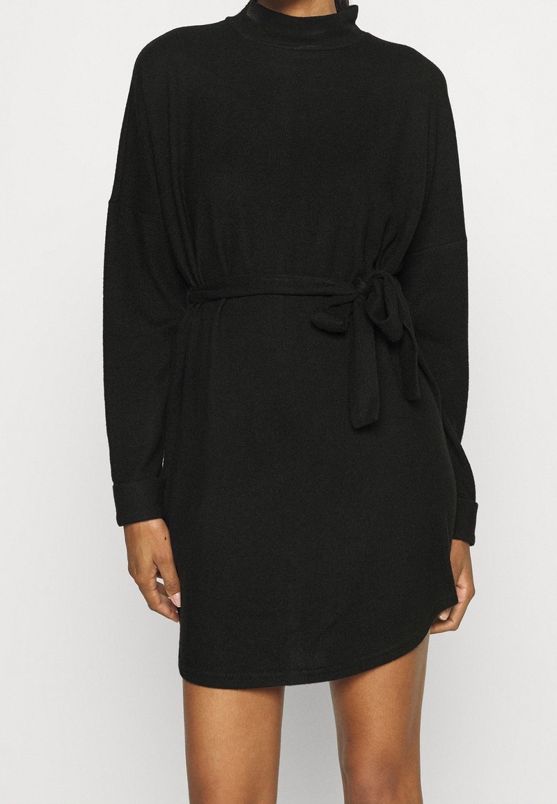 Robe noire à manches longues avec un col montant et une taille ceinturée. Fabriquée en tissu doux, elle présente une coupe décontractée et sans motifs visibles.