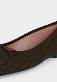 Gros plan sur une ballerine plate tressée marron foncé avec un petit nœud et une doublure intérieure rose pâle.