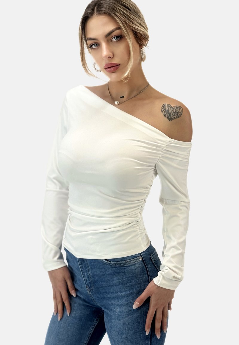 Witte off-shoulder top met lange mouwen, gerimpeld detail bij de taille, gemaakt van een gladde, rekbare stof. Gecombineerd met blauwe jeans.