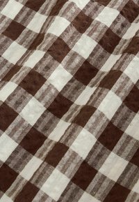 Braun-weiß kariertes Gewebe mit leicht zerknitterter Textur und sichtbarem Webmuster.