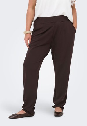Donna che indossa pantaloni larghi marrone scuro con tasche, abbinati a ballerine marrone scuro e una maglia bianca con maniche in pizzo.