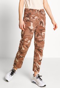 Kamouflage cargobyxor i nyanser av brunt och beige med avslappnad passform, utrustade med sidfickor och knappstängning för säker användning.
