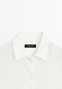White button-up shirt featuring a classic collar and a smooth texture, with a black label reading "Massimo Dutti" at the neckline.