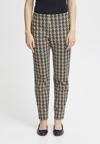 Pantaloni a punta di diamante beige e neri con vestibilità slim e lunghezza alla caviglia, realizzati in tessuto testurizzato. Abbinati a ballerine nere.
