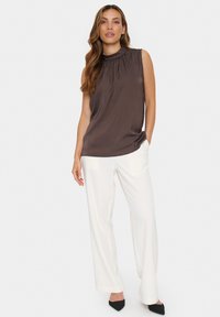 Top marrone senza maniche con scollatura arricciata, abbinato a pantaloni bianchi a gamba larga e scarpe nere a punta. Tessuto morbido, vestibilità rilassata.