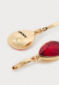 Orecchini in tonalità oro con forma a goccia; uno solido e uno con una pietra preziosa rossa sfaccettata, entrambi con chiusure a cerniera.