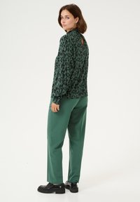 Maglietta a maniche lunghe con un motivo astratto nero e verde e un'apertura sul retro, abbinata a pantaloni verdi a vestibilità ampia e scarpe con plateau nere.