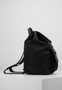 Black fabric backpack with a smooth texture, roll-top design, adjustable straps, and a small front pocket with a flap closure.