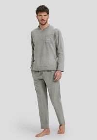 Conjunto de loungewear gris en tejido suave, que incluye una camiseta de manga larga con un bolsillo en el pecho y pantalones a juego de corte relajado.