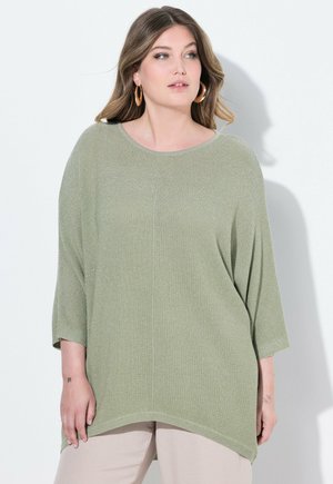 Pull large vert clair avec un design de tricot texturé, un col rond et des manches trois-quarts. Associé à un pantalon clair.