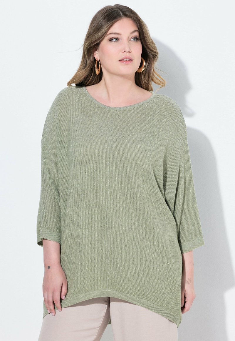 Maglione oversize verde chiaro con un design in maglia testurizzata, scollo rotondo e maniche a tre quarti. Abbinato a pantaloni di colore chiaro.
