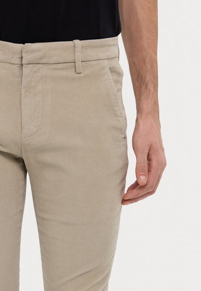 Pantaloni in corduroy beige con una vestibilità slim, dotati di tasche laterali e una sottile texture a righe, abbinati a un top nero.