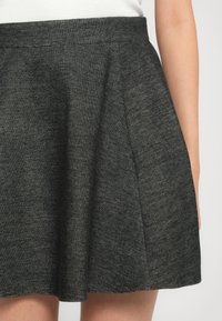 Jupe texturée gris foncé portée avec un haut blanc, mettant en valeur la taille et la partie supérieure de la jambe.