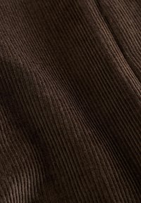 Barna kordbársony anyag, jellegzetes függőleges bordákkal, puha tapintással és gazdag színvilággal, amely meleg, tapintható minőséget hangsúlyoz.