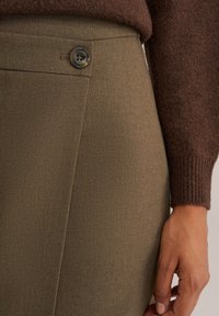 Pantaloni sagomati verde oliva con una texture liscia, tasche laterali e un bottone in vita per la chiusura.