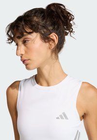 Biele športové tielko bez rukávov, hladká tkanina, okrúhly výstrih, s šedým logom a diagonálnym detailom na prednej strane, priliehavý strih.