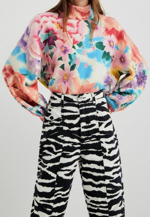 Femme portant un pull à col roulé fleuri coloré avec des manches bouffantes et un pantalon taille haute à imprimé zèbre noir et blanc.