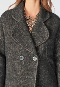 Cappotto doppiopetto in grigio scuro a spina di pesce. Realizzato in tessuto testurizzato, con due bottoni blu e colletto a risvolto.