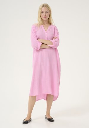 Vestido rosa de manga larga y botones con un corte relajado y un dobladillo asimétrico. Confeccionado en tela ligera con un acabado texturizado. Zapatos planos negros.