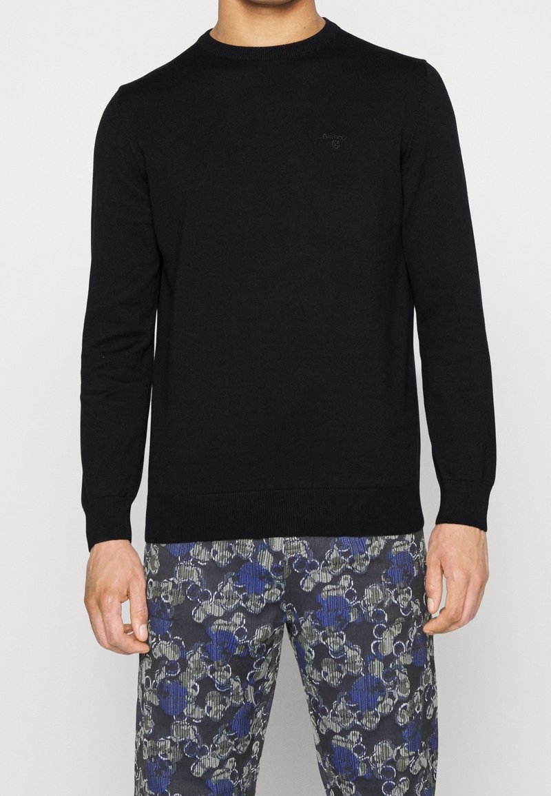 Pull en maille noire avec encolure ronde et manches longues. Présente un détail de logo subtil sur la poitrine ainsi que des poignets et un ourlet côtelés.