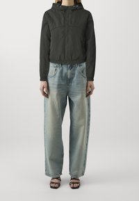 Svart kort jacka med huva, elastisk midja, kombinerad med bleka blå vida jeans och svarta sandaletter med remmar. Släta tygtexturer.