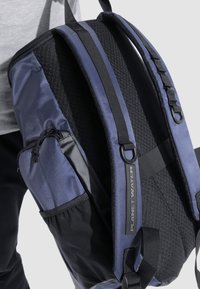 Sort og marineblå rygsæk med struktureret overflade, justerbare stropper, en sidelomme og et logo-tag. Holdbart materiale og sporty design.