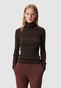 Maglione a collo alto a coste marrone con maniche lunghe, design aderente e texture liscia. Abbinato a pantaloni marroni a vita alta.