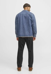 Lichte blauwe denimjack met een knoopsluiting aan de voorkant, zijzakken en een puntige kraag. Gepaard met zwarte broeken en bruine laarzen.
