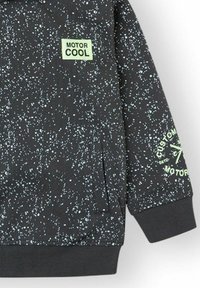 Sudadera negra con un patrón moteado en blanco y azul claro. Presenta la etiqueta "MOTOR COOL" y el texto "CUSTOM MOTOR" en la manga. Tiene bolsillos.
