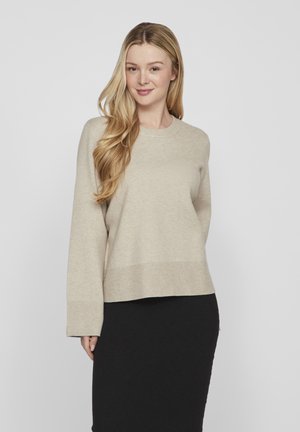 Beige Pullover aus weichem Stoff mit Rundhalsausschnitt und langenÄrmeln, mit gerippten Bündchen und Saum. Getragen mit einem schwarzen Rock.