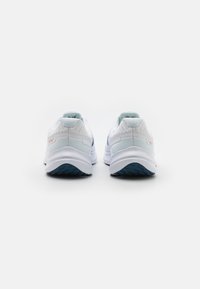 Zapatillas deportivas blancas con una parte superior de malla texturada, suela azul y sutiles acentos rosas en el talón. Diseñadas para la comodidad y el soporte.