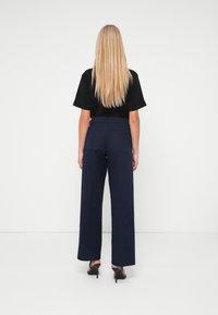 Černý top s krátkým rukávem v kombinaci s vysokými, širokými kalhotami navy barvy. Tento outfit má hladkou texturu a zadní kapsy.