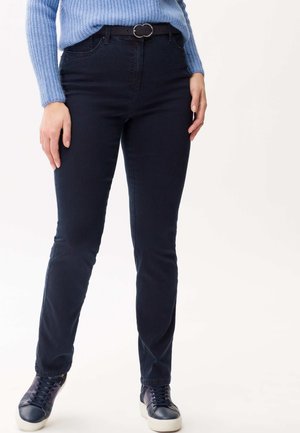 Marineblaue Skinny Jeans mit einer glatten Textur, kombiniert mit einem hellblauen gerippten Pullover und dunklen Sneakers. Enthält einen schwarzen Gürtel mit einer runden Schnalle.