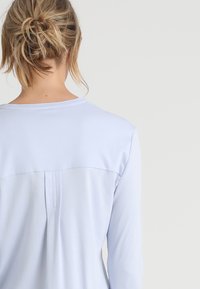 Světle modrá košile s dlouhými rukávy s zadním dílem a detailem sklady, vyrobená z měkké tkaniny s hladkým povrchem. Žádné výrazné kovové prvky.