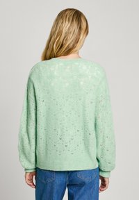 Piparmētru zaļš adīts džemperis ar brīvu piegriezumu, garām piedurknēm un teksturētu dimanta rakstu. Valkāts virs ziliem džinsiem.