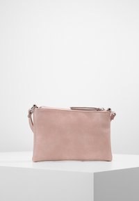 Malý růžový kožený zápěstní pouzdro s zipovým uzávěrem, vystavené na bílém geometrickém podstavci proti jednobarevnému pozadí.