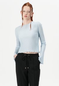 Lysblå ribbet langærmet top med cropped skæring og flared ærmer, parret med sorte bukser med snoretræk. Glat tekstur, tætsiddende design.