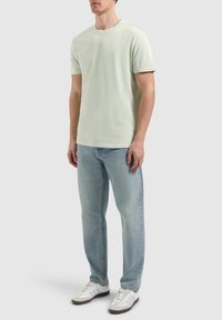 Lichtgroene katoenen T-shirt met korte mouwen, ronde hals, gecombineerd met lichtblauwe jeans en witte sneakers met grijze accenten.