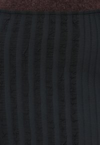 Tela negra texturizada con rayas verticales y un diseño con volantes. La sección superior muestra un material sólido de color marrón oscuro parecido a la lana.