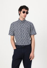 Camicia a maniche corte di colore blu navy con un motivo di foglie bianche. Presenta un colletto con bottoni, una vestibilità slim ed è abbinata a pantaloni scuri.